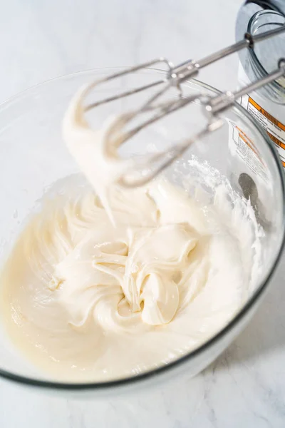 Mixing ingredients in a large glass mixing bowl to make the cream cheese glaze.
