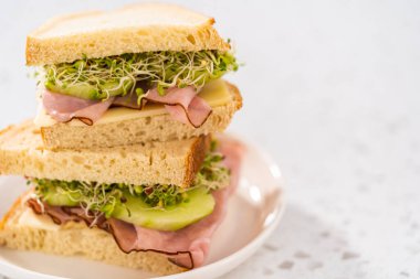 Stack of ham, cucumber, and sprout sandwiches on the white plate