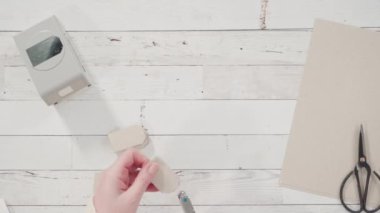 Düz yatıyordu. Adım adım. Kahverengi kağıttan hediye etiketlerini kağıt punçla kesiyor..