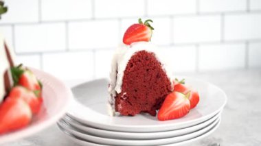 Step by step. Slicing red velvet bundt cake with cream cheese frosting garnished with fresh strawberries.