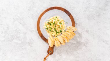 Flat lay. Assembling butter board with vegetables and bread on a round wood cutting board.