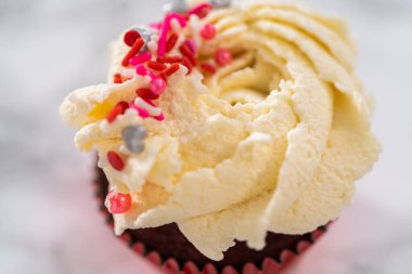 Kırmızı kadife keklerin üstüne beyaz çikolatalı ganache süsleme ve üzerine de çikolata parçacıkları serpiştirme..