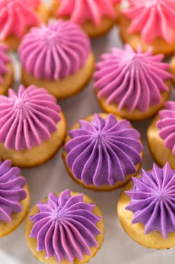 Beyaz pasta standında pembe tereyağlı taze pişmiş mini vanilyalı kekler..