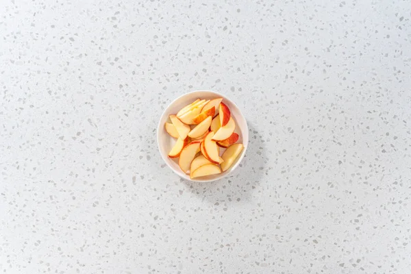 İnce dilimlenmiş kırmızı elmalar beyaz bir tabakta.