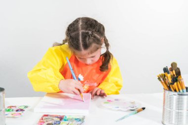 Evde akrilik boyalı bir sanat projesi üzerinde çalışan küçük bir kız..
