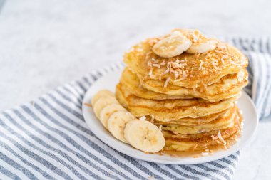 Dilimlenmiş muz, kızarmış hindistan cevizi ve akçaağaç şurubuyla süslenmiş taze hindistan cevizli krep yığını..