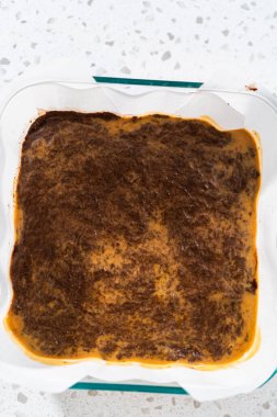 Çikolatalı fıstık ezmeli şekerleme hazırlamak için parşömen kağıdıyla kaplı fırın tavasına şekerleme döküyorum..