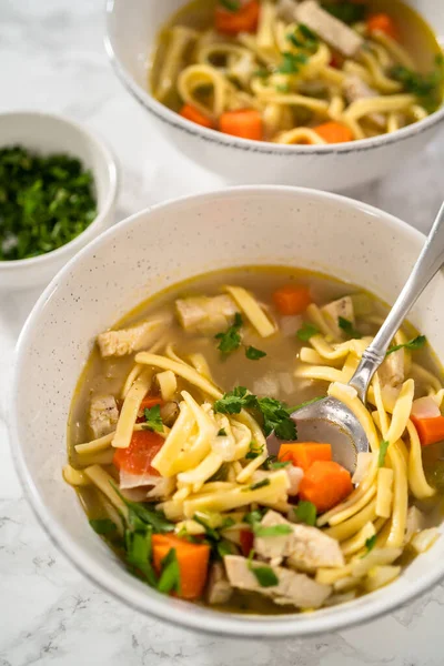 Serving chicken noodle soup with kluski noodles in white ceramic soup bowls.