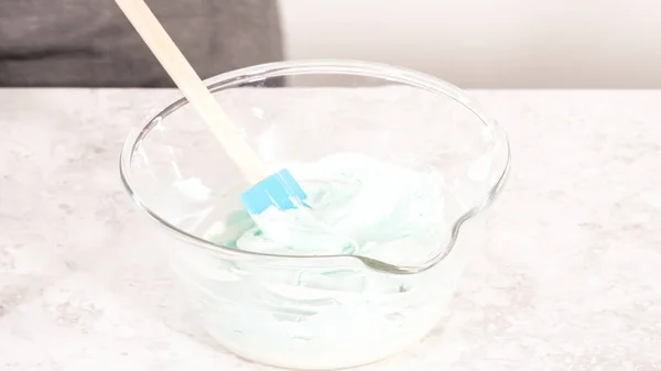 Step by step. Mixing in blue food coloring into the buttercream frosting.