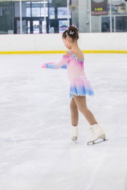 Küçük kız buz pateni pistinde artistik patinaj yapıyor..