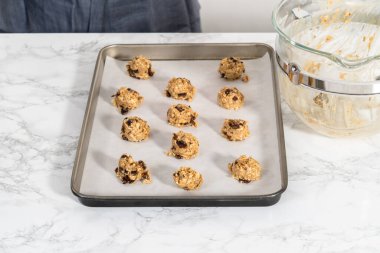 Yumuşak yulaf ezmeli, cevizli, kuru üzümlü kurabiye pişirmek için parşömen kağıdıyla kaplı bir yemek tepsisine hamur kepçesiyle kurabiye pişirmek..