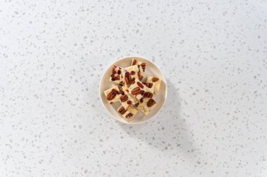 Düz yatıyordu. Beyaz seramik tabakta ev yapımı beyaz çikolatalı fındıklı şekerleme parçaları..