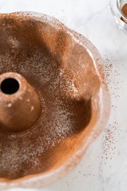Greasing metal bundt cake pan with vegetable shortening and cocoa powder to bake gingerbread bundt cake with caramel filling.