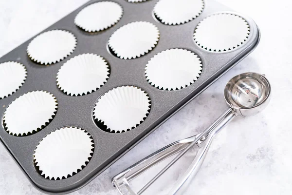 Lining cupcake baking pan with foil cupcake liners to bake unicorn rainbow chocolate cupcakes.