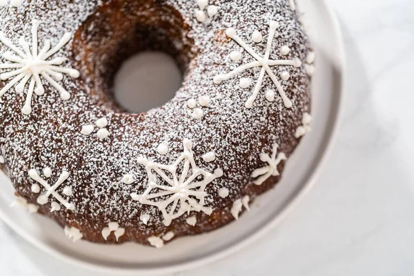 Gingerbread bundt cake with caramel filling, buttercream frosting, and powdered sugar dusting on the kitchen counter.