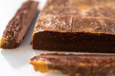 Çikolatalı fıstık ezmeli şekerlemeyi beyaz bir kesme tahtasında küçük parçalara ayırmak..