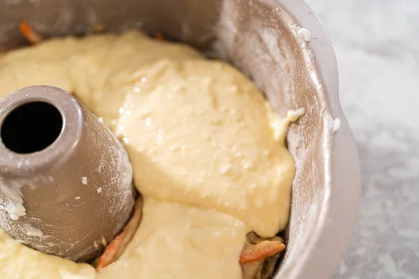 Filling metal bundt cake pan with cake butter to bake carrot bundt cake with cream cheese frosting.