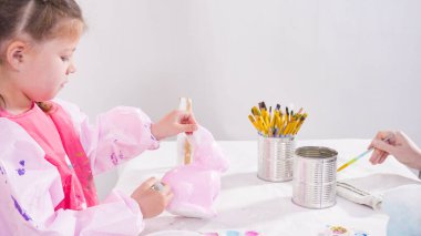 Küçük kız evde eğitim projesi için akrilik boyayla heykelcikler boyuyor..