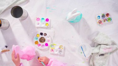 Düz yatıyordu. Küçük kız evde eğitim projesi için akrilik boyayla heykelcikler boyuyor..