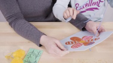 Küçük kız annesiyle el sanatları masasında dikiş dikmeyi öğreniyor..