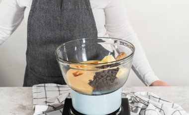 Beyaz çikolata parçacıkları ve diğer malzemeleri kaynayan suyun üzerine karıştırıp çikolatalı macadamia şekerlemesi hazırlıyorum..