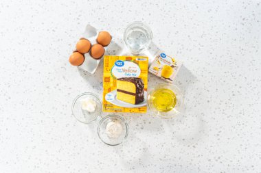 Düz yatıyordu. Kutu kekten basit bir vanilyalı kek pişirmek için cam karışımında ölçülmüş malzemeler..