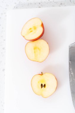 Kırmızı elmaları beyaz bir kesme tahtasının üzerinde ince dilimlere ayırmak.