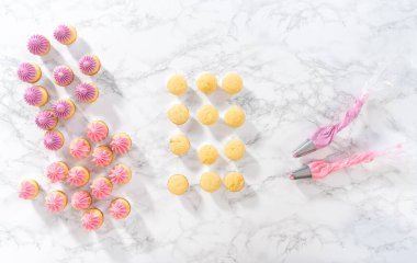 Düz yatıyordu. Mini vanilyalı keklerin üzerine pembe tereyağlı krema sıkıyorum..