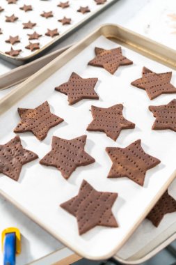 Fırınlanmamış yıldız şekilli çikolatalı krakerler, parşömen kağıdıyla kaplı fırın örtüsü üzerinde..