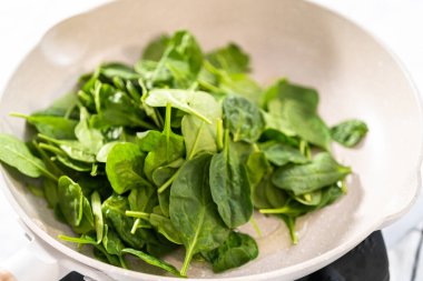 Ispanaklı sarımsaklı karides makarna hazırlamak için önemsiz bir tavada taze ıspanak kızartıyorum..