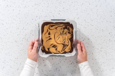 Düz yatıyordu. Fıstık ezmeli çikolatalı şekerlemeyi hazırlamak için parşömen kağıdıyla kaplı fırın tavasına şekerleme döküyorum..