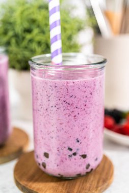 Freshly made mixed berry boba smoothie in a drinking jar with paper straw.