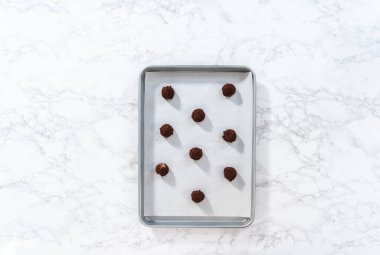 Flat lay. Scooping cookie dough with a small dough scoop into a baking sheet lined with parchment paper to bake peppermint white chocolate cookies.