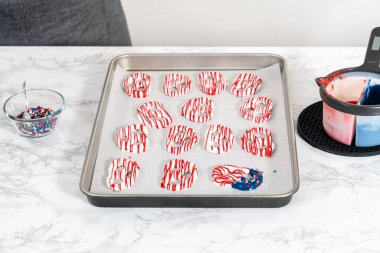 Flat lay. Dipping pretzels twists into melted chocolate to make red, white, and blue chocolate-covered pretzel twists.