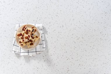 Düz yatıyordu. Beyaz seramik tabakta ev yapımı beyaz çikolatalı fındıklı şekerleme parçaları..