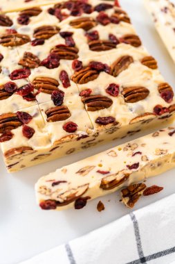 Beyaz çikolatalı fındıklı fındıklı şekerlemeyi beyaz bir kesme tahtasında küçük parçalara ayırmak..