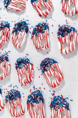 Dipping pretzels twists into melted chocolate to make red, white, and blue chocolate-covered pretzel twists.