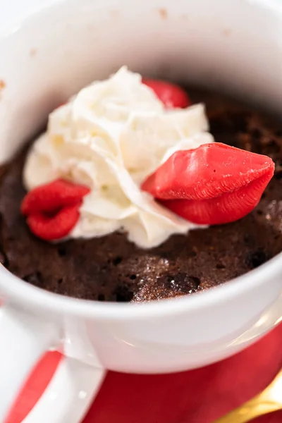 Chocolate mug cakes garnished with whipped cream and chocolate hearts and lips.
