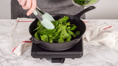 Adım adım. Ispanak ve jambonlu frittata hazırlamak için sobanın üzerinde dökme demir tava var..