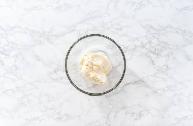 Flat lay. Whisking buttercream frosting in a glass mixing bowl with an electric hand mixer to prepare the peppermint buttercream frosting.