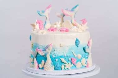 Deniz kızı temalı 3 katlı vanilyalı pasta çikolatalı deniz kızı kuyruğu ve deniz kabuğu ile süslenmiş beyaz pasta standı.