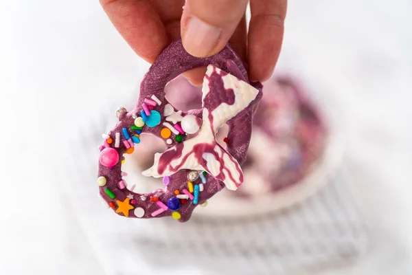 Homemade chocolate-dipped pretzel twists decorated with colorful sprinkles and chocolate mermaid tails on a white plate.