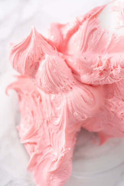 Mixing in store-bought buttercream frosting in a glass mixing bowl.