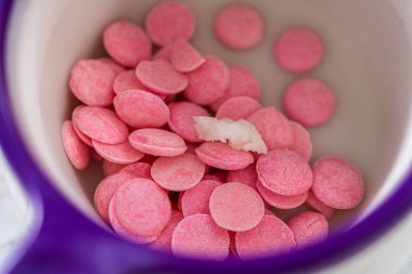 Panda şeklindeki kurabiyeler için çikolatalı fiyonk yapmak için şekerleme kabında pembe çikolata parçacıkları eritiyorum..