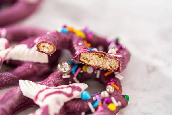 Homemade chocolate-dipped pretzel twists decorated with colorful sprinkles and chocolate mermaid tails on a white plate.