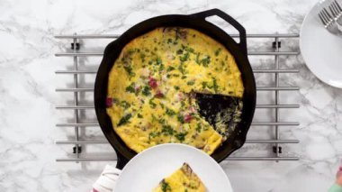 Flat lay. Slicing freshly baked spinach and ham frittata in cast iron skillet.