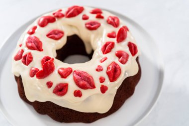 Freshly baked red velvet bundt cake with chocolate lips and hearts over cream cheese glaze for Valentines Day.