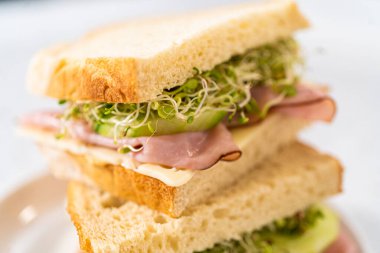 Stack of ham, cucumber, and sprout sandwiches on the white plate