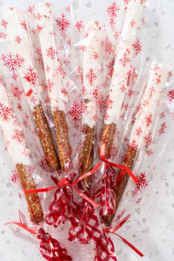 Packaging homemade candy cane chocolate-covered pretzel rods into clear plastic bags for Christmas gifts. clipart