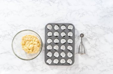 Flat lay. Scooping cupcake batter with dough scoop into a baking cupcake pan with liners to bake mini vanilla cupcakes with ombre pink buttercream frosting.